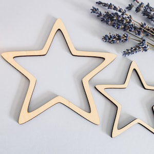 Peut inclure: Deux étoiles en bois, l'une plus grande que l'autre, sur un fond gris clair. Les étoiles sont non finies et ont une couleur bois naturelle.