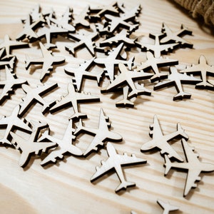 May include: A scattering of wooden airplane cutouts on a light wood surface. The airplanes are all the same size and shape, and they are arranged in a random pattern.