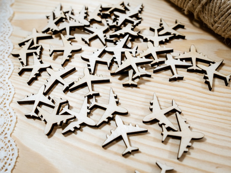 May include: A scattering of wooden airplane cutouts on a light wood surface. The airplanes are all the same size and shape, and they are arranged in a random pattern.