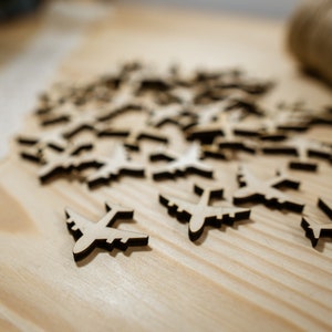 May include: A pile of wooden airplane cutouts on a light brown wooden surface. The airplanes are all the same size and shape, and they are arranged in a random pattern.