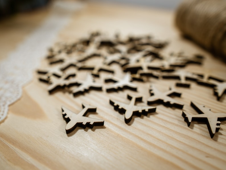 May include: A pile of wooden airplane cutouts on a light brown wooden surface. The airplanes are all the same size and shape, and they are arranged in a random pattern.