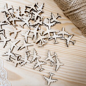 May include: A collection of wooden airplane cutouts scattered on a light wood surface. The airplanes are all the same size and shape, and they are arranged in a random pattern.