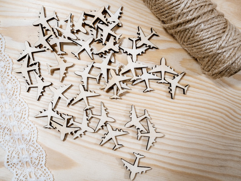 May include: A collection of wooden airplane cutouts scattered on a light wood surface. The airplanes are all the same size and shape, and they are arranged in a random pattern.