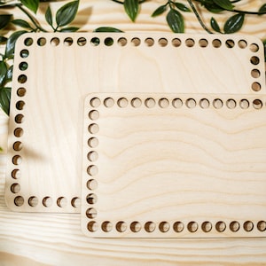 May include: Two wooden loom frames, one larger than the other, with holes around the edges. The frames are made of light wood and are sitting on a wooden surface.