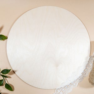Könnte beinhalten: Eine runde, unfertige Holzscheibe mit natürlicher Holzmaserung. Die Scheibe ist von einer weißen Spitzenborte und einer Rolle Schnur umgeben.