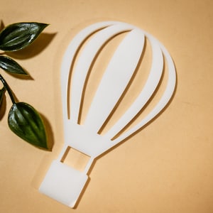 Puede incluir: Corte de papel blanco de un globo aerostático con un diseño simple. El globo tiene una parte superior redondeada y una base rectangular.