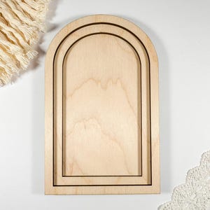 May include: A wooden archway with three concentric circles, creating a frame for displaying photos or other small items. The archway is made of natural wood and has a light brown colour.