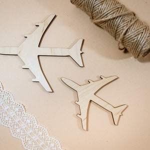May include: Two wooden airplane shapes on a light brown background. The airplanes are made of light wood and are in the shape of a traditional airplane.