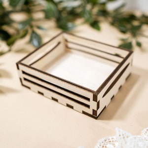 May include: A small wooden crate with a natural wood finish and dark brown edges. The crate is empty and has a rectangular shape.