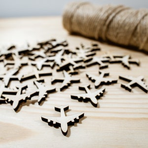 May include: A pile of wooden airplane cutouts on a light wood surface. The cutouts are all the same size and shape, and they are arranged in a random pattern.