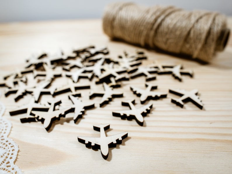 May include: A pile of wooden airplane cutouts on a light wood surface. The cutouts are all the same size and shape, and they are arranged in a random pattern.