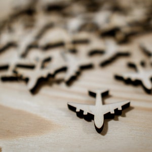 May include: A close-up of a wooden table with a scattering of small wooden airplane cutouts. One airplane is in focus and is positioned in the center of the image.