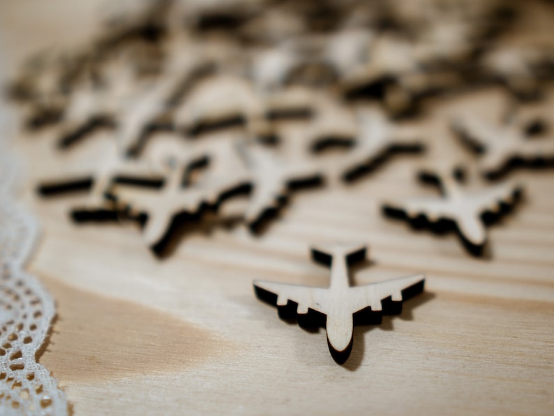 May include: A close-up of a wooden table with a scattering of small wooden airplane cutouts. One airplane is in focus and is positioned in the center of the image.