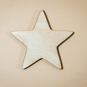 Può includere: Una stella di legno a cinque punte, presentata su uno sfondo neutro. La stella ha una venatura naturale e una finitura chiara non trattata, ideale per lavori artigianali e decorazioni.
