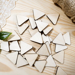 May include: A collection of unfinished wooden triangle shapes, scattered on a light wood surface. The triangles are various sizes and are perfect for crafting projects.