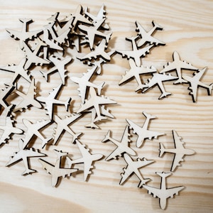 May include: A collection of wooden airplane shapes, scattered on a light wood surface. The airplanes are all the same size and shape, and they are arranged in a random pattern.