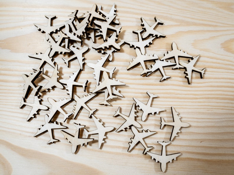 May include: A collection of wooden airplane shapes, scattered on a light wood surface. The airplanes are all the same size and shape, and they are arranged in a random pattern.