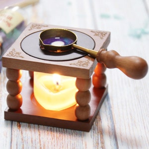 May include: A wooden wax seal kit with a small metal pot for melting wax, a wooden handle, and a candle. The pot is filled with purple wax and the candle is lit.