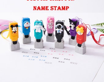 Puede incluir: Siete sellos de nombre rectangulares de plástico en amarillo, azul, turquesa, rosa, negro, morado y rojo, cada uno con una figura de dibujos animados diferente. El texto CUSTOM CARTOON NAME STAMP aparece sobre los sellos en una superficie blanca.