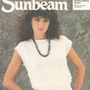 May include: A woman modelling a white knitted top with a textured pattern and a black and white beaded necklace. The top is paired with black and white striped trousers. The image includes the text "Sunbeam" and "813 Double Knitting Cotton".