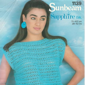 May include: A woman models a turquoise crochet top with a boat neck and cap sleeves. The top is paired with white trousers. The image includes the text "Sunbeam Sapphire D.K." and measurements of 71-107 cm.