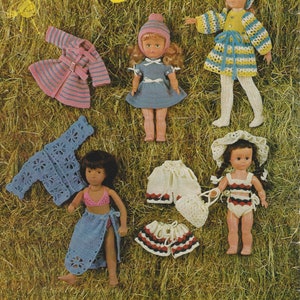 May include: A vintage "Dolly Book" cover featuring dolls and crochet doll clothing. The cover text reads "Dolly Book by Emu". The dolls are wearing various crocheted outfits in blue, pink, white, and yellow. The background is a field of dry grass.