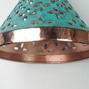 Close up view of of cone copper lights combining hand-carved cut-out pattern with green patina finish and small strip of hand-hammered pattern with polished copper finish, with natural copper finish interior.