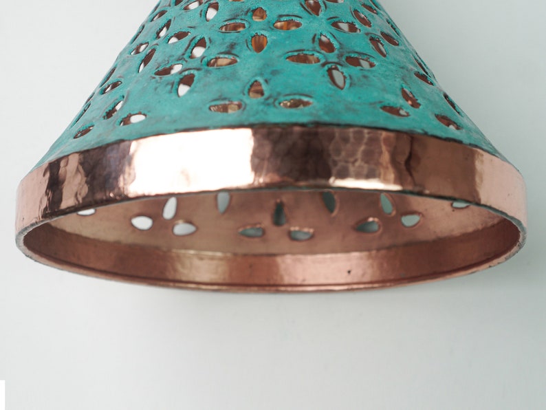 Close up view of of cone copper lights combining hand-carved cut-out pattern with green patina finish and small strip of hand-hammered pattern with polished copper finish, with natural copper finish interior.
