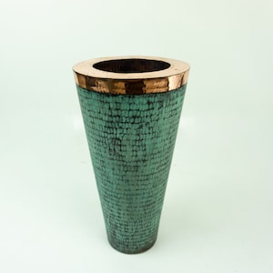 Könnte beinhalten: Eine handgefertigte Vase mit einer strukturierten, türkisfarbenen Außenseite und einem kupferfarbenen Rand. Die Vase hat eine weite Öffnung und eine konische Form, ideal für die Präsentation von Blumen oder als dekoratives Element. Die Vase ist aus Metall.