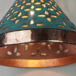 close up view of cone copper lights combining hand-carved cut-out pattern with green patina finish and small strip of hand-hammered pattern with polished copper finish, with natural copper finish interior.