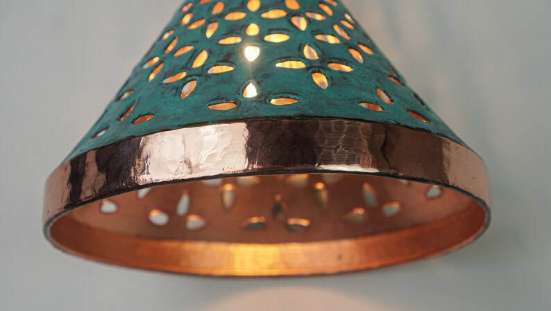 close up view of cone copper lights combining hand-carved cut-out pattern with green patina finish and small strip of hand-hammered pattern with polished copper finish, with natural copper finish interior.