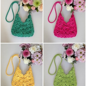May include: A collection of four crochet bags in emerald green, hot pink, yellow, and lime green. Each bag features a scalloped shell pattern, a matching braided shoulder strap, and a scalloped top edge, displayed alongside a bouquet of flowers.