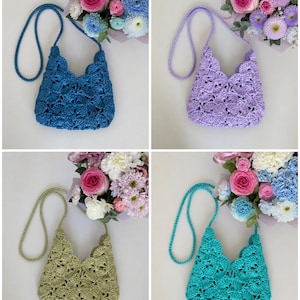 May include: A collection of four crochet bags in blue, lavender, sage green, and turquoise. Each bag features a scalloped shell pattern, a matching braided shoulder strap, and a V-shaped top opening, displayed alongside a bouquet of flowers.