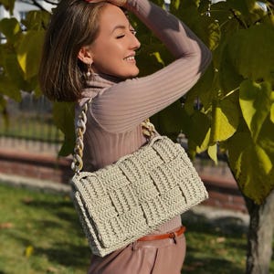 May include: A rectangular crochet handbag in a light beige color featuring a woven basket-weave pattern and a thick, chunky chain-link handle made of marbled cream and tan acrylic links, attached to the bag with silver-toned metal hardware.