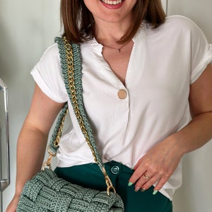 May include: A sage green woven handbag featuring a thick, textured basket-weave pattern and a gold-tone metal chain shoulder strap. The rectangular bag has a flap closure and is constructed from a sturdy, cord-like material in a muted green tone.