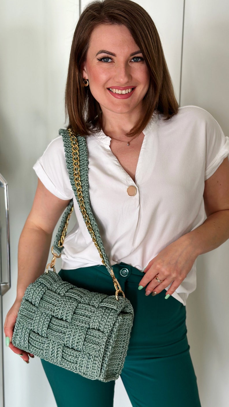 May include: A sage green woven handbag featuring a thick, textured basket-weave pattern and a gold-tone metal chain shoulder strap. The rectangular bag has a flap closure and is constructed from a sturdy, cord-like material in a muted green tone.