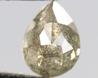 Puede incluir: Un diamante gris en forma de pera, facetado, con inclusiones. El diamante está sujeto por unas pinzas.