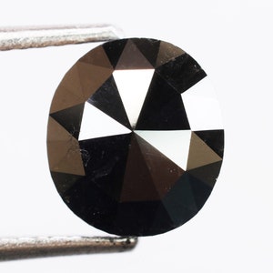 Puede incluir: Un diamante redondo negro con corte facetado. El diamante está sujeto con unas pinzas.