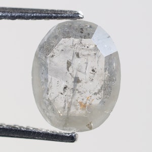 May include: A clear, faceted, oval-shaped diamond with inclusions. The diamond is held by tweezers.