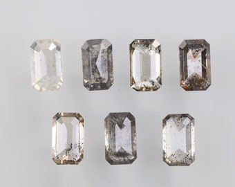 May include: Seven rectangular-cut gemstones with varying shades of gray and clear facets are displayed against a white background. The gemstones have a symmetrical, elongated shape, with visible inclusions and imperfections.