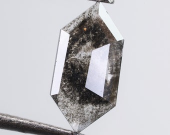 Może przedstawiać: Szlifowany, sześciokątny diament szary z czarnymi inkluzjami. Diament jest trzymany w pęsecie.