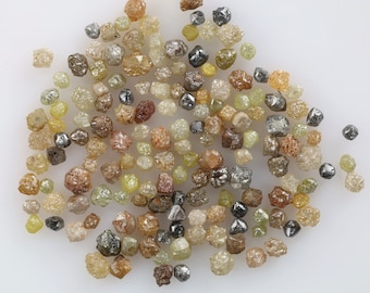 May include: A collection of small, rough, uncut diamonds in various shades of brown, yellow, and grey. The diamonds are scattered on a white surface.