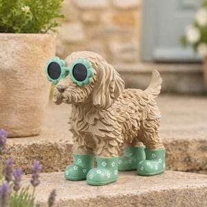 May include: A decorative dog statue wearing flower-shaped sunglasses and green wellington boots. The dog is light brown with textured fur. The boots, adorned with a white floral pattern, add a playful touch to the garden. The statue is on a stone step.