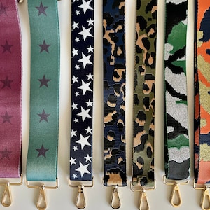 May include: Seven different fabric straps with gold metal clasps. The straps feature various patterns including stars, leopard print, and camouflage.
