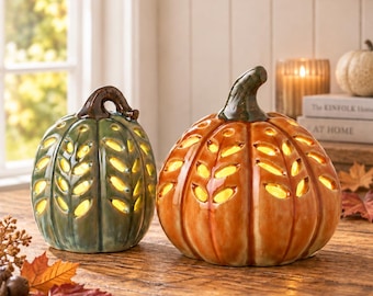 May include: Two ceramic pumpkin-shaped lanterns with a glossy finish. One is green and the other is orange, both featuring cut-out leaf patterns that emit a warm yellow light from within. Each pumpkin has a dark brown stem on top.