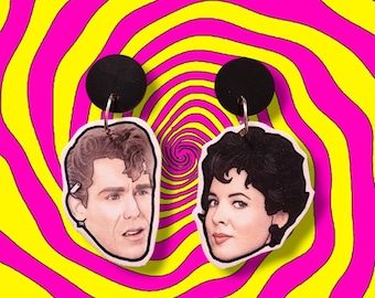 May include: A pair of dangle earrings featuring the faces of two people. The earrings are made of white material and have black backing. The faces are printed with realistic details.