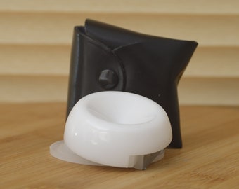 May include: A white plastic ring holder with a black leather case. The ring holder has a smooth, rounded surface and a small, flat base.