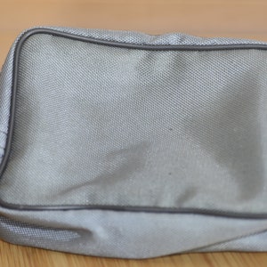 May include: A gray zippered pouch with a black zipper and black trim. The pouch is made of a soft, textured fabric.