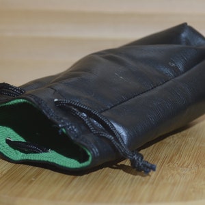 May include: A black leather drawstring bag with a green lining. The bag is lying on a wooden surface.