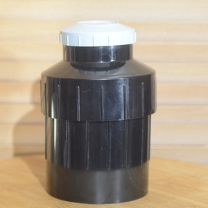 Może przedstawiać: Czarny plastikowy pojemnik z białą pokrywką. Pojemnik ma żebrowaną konstrukcję i służy do przechowywania filmu.